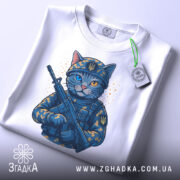 Футболка котик герой, складена біла футболка з принтом кота в військовій формі, з автоматом, фон світлий, на футболці видно етикетку з зеленим шнурком, деталі принта яскраві.