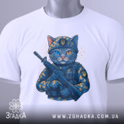 Футболка котик герой, складена біла футболка з принтом кота в військовій формі, з автоматом, фон світлий, на футболці видно етикетку з зеленим шнурком, деталі принта яскраві.