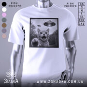 Футболка котик і НЛО, біла футболка на манекені, зображення кота з відкритим ротом і піднятою лапою, на фоні видно НЛО, принт в чорній рамці, фон світлий.