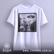 Футболка котик і НЛО, біла футболка на вішалці, зображення кота з відкритим ротом і піднятою лапою, на фоні видно НЛО, принт в чорній рамці, фон світлий.