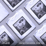 Футболка котик і НЛО, біла футболка на манекені, зображення кота з відкритим ротом і піднятою лапою, на фоні видно НЛО, принт в чорній рамці, фон світлий.