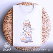 Футболка котики кумедні, біла, складена на плетеному кошику, фон світло-сірий, принт з трьома котиками, один оранжевий, один білий, один з оранжевими плямами, з написами 'No Speak', 'No Hear', 'No See'.