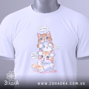 Футболка котики кумедні, біла, складена на столі, фон світло-сірий, принт з трьома котиками, один оранжевий, один білий, один з оранжевими плямами, з написами 'No Speak', 'No Hear', 'No See', на ярлику зелена стрічка.