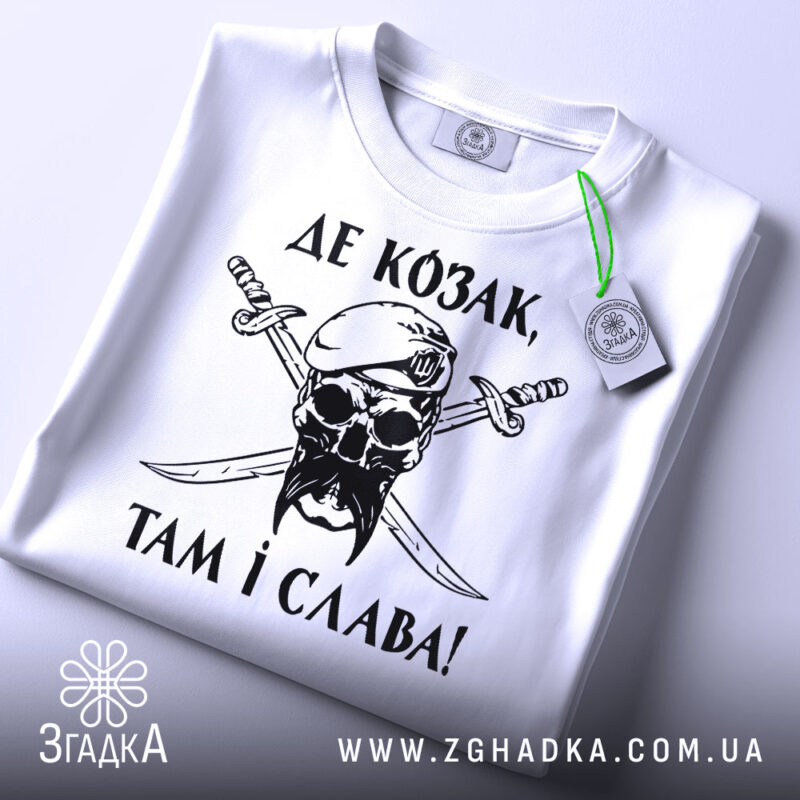 Футболка козак і слава, біла футболка, складена на поверхні, зображена з верхнього ракурсу, фон світло-сірий, принт чорного кольору з черепом у беретці та двома мечами, текст українською мовою, на футболці є етикетка з зеленим шнурком.