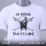 Футболка козак і слава, біла футболка, складена на поверхні, зображена з верхнього ракурсу, фон світло-сірий, принт чорного кольору з черепом у беретці та двома мечами, текст українською мовою, на футболці є етикетка з зеленим шнурком.