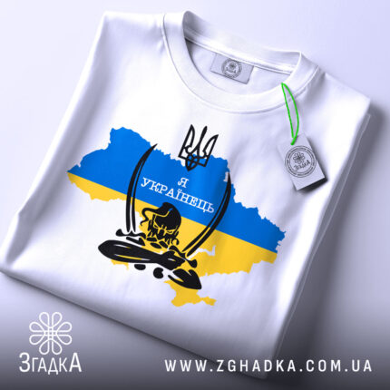 Футболка козак я українець, біла, складена на поверхні, фон світлий, принт з тризубом та написом 'Я УКРАЇНЕЦЬ' на фоні карти України в жовто-блакитних кольорах, з зеленим ярликом.