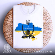 Футболка козак я українець, біла, складена на кошику, фон світлий, принт з тризубом та написом 'Я УКРАЇНЕЦЬ' на фоні карти України в жовто-блакитних кольорах.