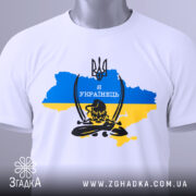 Футболка козак я українець, біла, складена на поверхні, фон світлий, принт з тризубом та написом 'Я УКРАЇНЕЦЬ' на фоні карти України в жовто-блакитних кольорах, з зеленим ярликом.