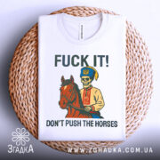 Футболка козак не жени. Біла футболка, складена на кошику, з принтом, що зображує скелета в українському вбранні на коні. На фоні світло-сірий градієнт. Текст на футболці: 'FUCK IT! DON'T PUSH THE HORSES'.