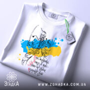 Футболка козацька воля, біла, складена на столі, фон світло-сірий, принт з козацьким воїном на фоні жовто-блакитних плям, текст українською мовою, з зеленим ярликом.