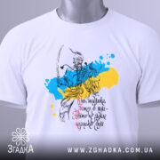 Футболка козацька воля, біла, складена на столі, фон світло-сірий, принт з козацьким воїном на фоні жовто-блакитних плям, текст українською мовою, з зеленим ярликом.