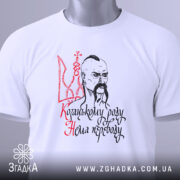 Футболка козацькому роду нема переводу. Біла футболка, складена на поверхні, зображена з верхнього ракурсу. На футболці видно принт з козацьким малюнком та написом, а також зелену етикетку.