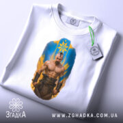 Футболка козацький дух, біла, зображена на столі, фон світло-сірий, принт з зображенням чоловіка з мускулатурою, на футболці є етикетка.