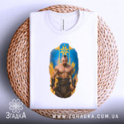 Футболка козацький дух, біла, зображена на столі в круглій кошику, фон білий, принт з зображенням чоловіка з мускулатурою на фоні жовто-блакитного щита.