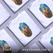 Футболка козацький дух, біла, зображена на манекені, фон світло-сірий, принт з зображенням чоловіка з мускулатурою на фоні жовто-блакитного щита.