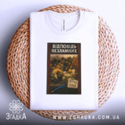 Футболка козацький гумор лист, біла футболка, складена на плетеному кошику, з принтом на грудях, який зображає картину з групою людей, що обговорюють щось, на фоні світло-сірий колір, принт оформлений в рамці з червоним узором.