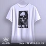 Футболка краса без ілюзій, білого кольору, підвішена на вішалці, фон світло-сірий, принт з черепом та написом 'BEAUTY' розташований по центру, виглядає стильно.