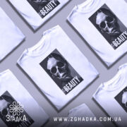 Футболка краса без ілюзій, білого кольору, зображена з фронтального ракурсу на манекені, фон світло-сірий, принт зображає череп та напис 'BEAUTY' на чорному фоні.