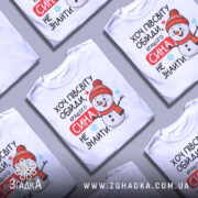 Футболка кращого сина. Біла футболка з принтом, на якому зображений смішний сніговик у червоній шапці та шарфі. Принт містить текст "Хочу півсвіту обійди, кращого сина не знайти". Фон нейтральний, злегка сірий, що підкреслює яскравість кольорів принта.