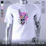 Футболка крейзі заєць, біла, зображена на манекені, фон світло-сірий, принт з веселим зайцем з короною, яскраві кольори, деталі принта включають рожеві та жовті елементи.