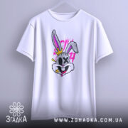 Футболка крейзі заєць, біла, підвішена на вішалці, фон світло-сірий, принт з зайцем з короною, яскраві кольори, деталі принта включають рожеві та жовті елементи.