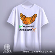 Футболка круасан стиль, біла, підвішена на вішалці, фон світло-сірий, принт з оранжевим круасаном та текстом 'PRASHANT CROISSANT' чорного кольору з зеленим галочкою.