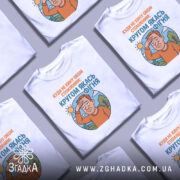 Футболка кругом якась фігня, біла футболка на манекені, ракурс спереду, фон нейтральний, принт з зображенням чоловіка з рудим волоссям, який прикриває очі від сонця, текст зверху оранжевого кольору, текст внизу блакитного кольору.