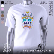 Футболка крихітка може все. Біла футболка з кольоровим принтом, зображеним на грудях, на фоні світло-сірого градієнту. Принт містить текст "ЦЯ КРИХІТКА МОЖЕ ВСЕ!" оточений кольоровими елементами, такими як зірочки та листя.