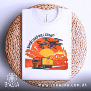 Футболка кримський міст горить, біла, складена на плетеній основі, фон нейтральний, принт зображає вантажівку та дрони на фоні палаючого мосту з оранжевими та червоними відтінками.