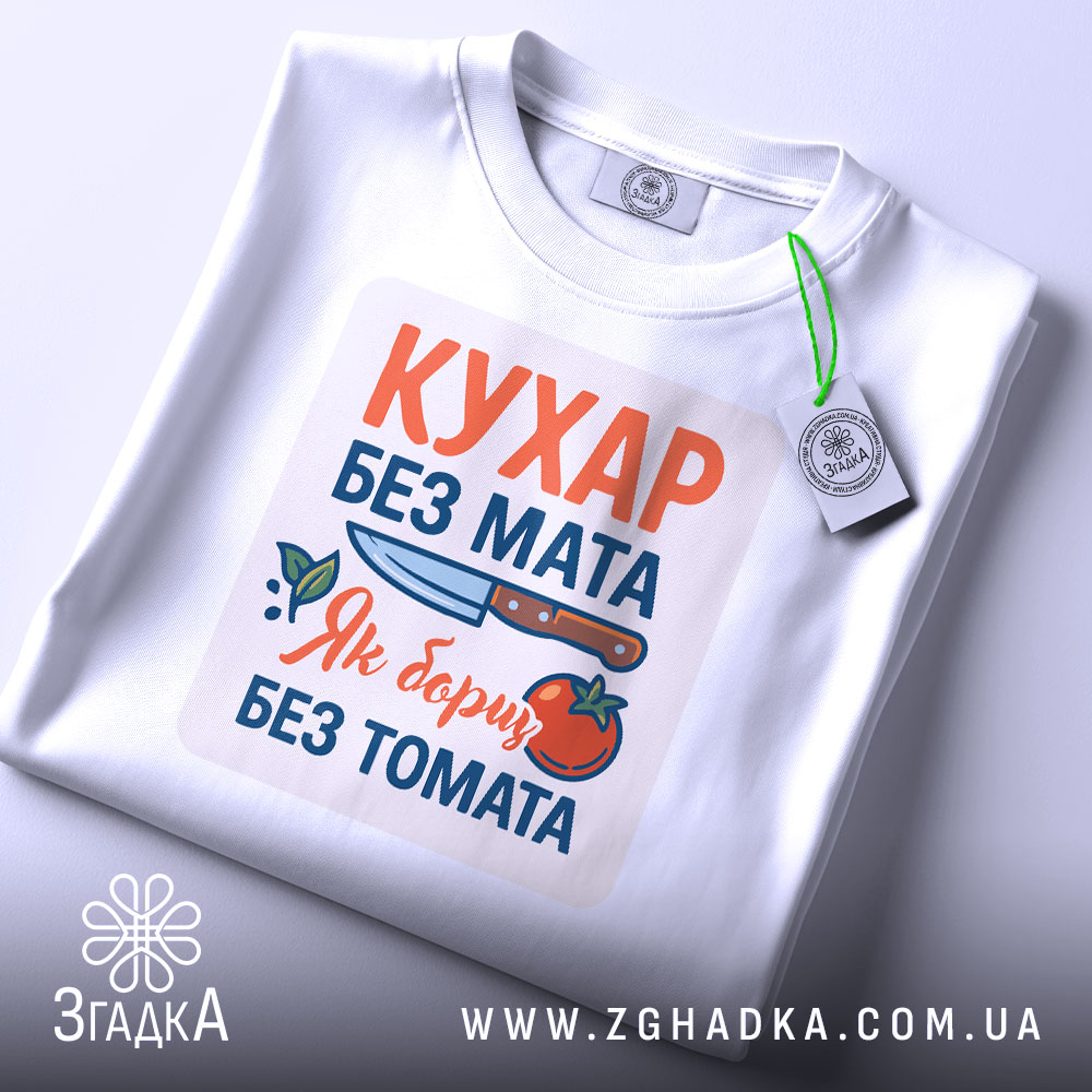 Футболка кухар без мата, біла, зображена зверху, фон світло-сірий, принт містить текст "КУХАР БЕЗ МАТА" з ілюстрацією ножа та помідора, на футболці є етикетка.