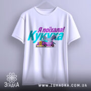 Футболка кукуха поїхала, біла, зображена з фронтального ракурсу, на фоні світло-сірого кольору, принт містить текст "Я поїхала! Кукуха" та малюнок автомобіля з птахом, футболка висить на вішалці.