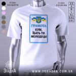 Футболка кум молодець. Біла футболка з коротким рукавом, зображена з фронтального ракурсу. На фоні світло-сірий градієнт. Принт містить текст 'ГРАМОТА КУМ, ІБАТЬ ТИ МОЛОДЕЦЬ!' у синьому та чорному кольорах, а також герб України та жовто-блакитні стрічки.