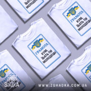 Футболка кум молодець. Біла футболка з коротким рукавом, зображена з фронтального ракурсу. На фоні світло-сірий градієнт. Принт містить текст 'ГРАМОТА КУМ, ІБАТЬ ТИ МОЛОДЕЦЬ!' у синьому та чорному кольорах, а також герб України та жовто-блакитні стрічки.