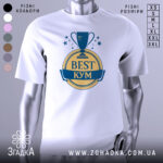Футболка кум найкращий, біла, зображена з фронтального ракурсу на манекені, фон світло-сірий, принт з трофеєм та написом 'BEST КУМ' у жовтому та синьому кольорах.