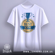 Футболка кум найкращий, біла, зображена з фронтального ракурсу на вішалці, фон світло-сірий, принт з трофеєм та написом 'BEST КУМ' у жовтому та синьому кольорах.