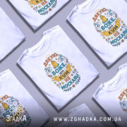 Футболка кум не москаль, біла, зображена на манекені, фон світло-сірий, принт з текстом "Дякую, Боже, що кум не москаль!" в яскравих кольорах, з елементами декору.