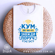 Футболка кум завжди поруч, біла, зображена зверху на плетеній основі, фон світлий, принт з текстом "КУМ ЯК WI-FI ЗАВЖДИ ПОРУЧ" у жовтому та блакитному кольорах, оформлений декоративними елементами.