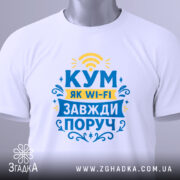 Футболка кум завжди поруч, біла, зображена зверху, фон світлий, принт з текстом "КУМ ЯК WI-FI ЗАВЖДИ ПОРУЧ" у жовтому та блакитному кольорах, на футболці є етикетка з логотипом.