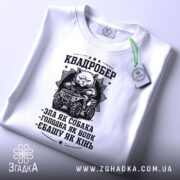 Футболка квадробер білого кольору, складена на поверхні, з видимим ярликом, фон світло-сірий, принт чорного кольору з котом на квадроциклі та текстом.