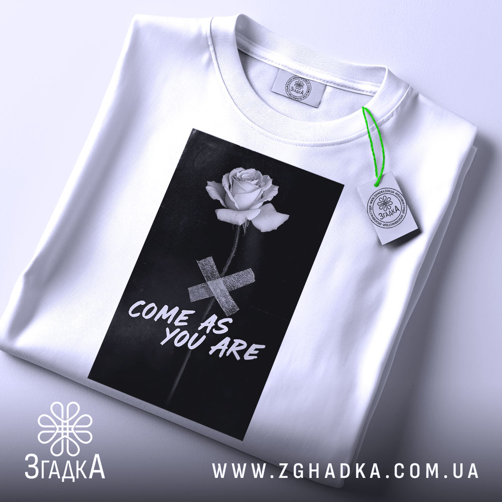 Футболка квітка монохром, біла, складена на поверхні, фон світло-сірий, принт з чорним фоном, білою трояндою та написом 'COME AS YOU ARE', з етикеткою зеленого кольору.