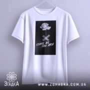 Футболка квітка монохром, біла, підвішена на вішалці, фон світло-сірий, принт з чорним фоном, білою трояндою та написом 'COME AS YOU ARE'.