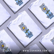 Футболка квітка ромашка, біла, зображена на манекені з правого ракурсу, фон нейтральний, принт з ромашкою та написом 'GOOD VIBES' у кольоровій палітрі.