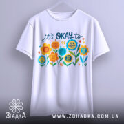 Футболка квіткова мотивація. Біла футболка, підвішена на вішалці, з кольоровим принтом на грудях. Принт включає різнокольорові квіти та текст, що закликає до позитивного мислення. Фон світло-сірий, що підкреслює яскравість кольорів принта.