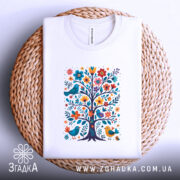 Футболка квіткове дерево, біла, складена на плетеній кошику, фон світлий, принт з кольоровим деревом, птахами та квітами.