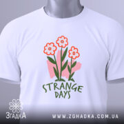 Футболка квіткові арт дні, біла, зображена зверху, складена на поверхні, фон світло-сірий, принт з трьома червоними квітами та написом 'STRANGE DAYS' зеленого кольору, з етикеткою.