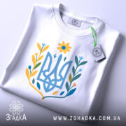 Футболка квітковий тризуб, біла, складена на поверхні, фон світло-сірий, принт у вигляді тризуба з квітковими елементами в жовтих, блакитних та зелених відтінках, з етикеткою, що звисає.