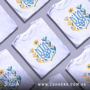 Футболка квітковий тризуб, біла, зображена з правого ракурсу на манекені, фон світло-сірий, принт у вигляді тризуба з квітковими елементами в жовтих, блакитних та зелених відтінках.