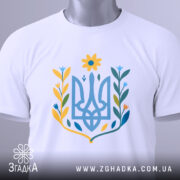 Футболка квітковий тризуб, біла, складена на поверхні, фон світло-сірий, принт у вигляді тризуба з квітковими елементами в жовтих, блакитних та зелених відтінках, з етикеткою, що звисає.