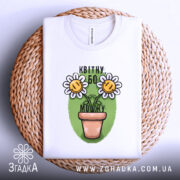 Футболка квітну бо можу, білого кольору, складена на плетеному кошику, фон білий, принт з двома усміхненими соняшниками в горщику на зеленому фоні.