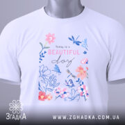 Футболка квіти прекрасний день, складена футболка на білому фоні, вид зверху, принт з квітами та метеликами в пастельних кольорах, текст "Today is a BEAUTIFUL day" розташований в центрі, з етикеткою на зеленому шнурку.